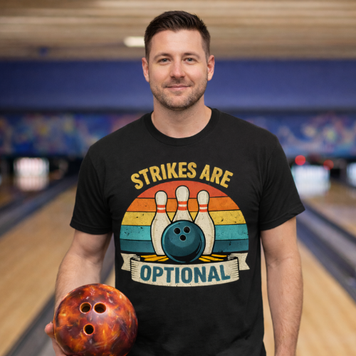 Man wearing a black t-shirt with a bowling design holding a bowling ball in a bowling alley.